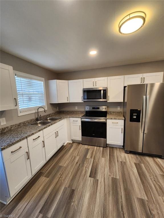 kitchen featuring sink, dark stone countertops, white cabinets, dark hardwood / wood-style flooring, and stainless steel appliances