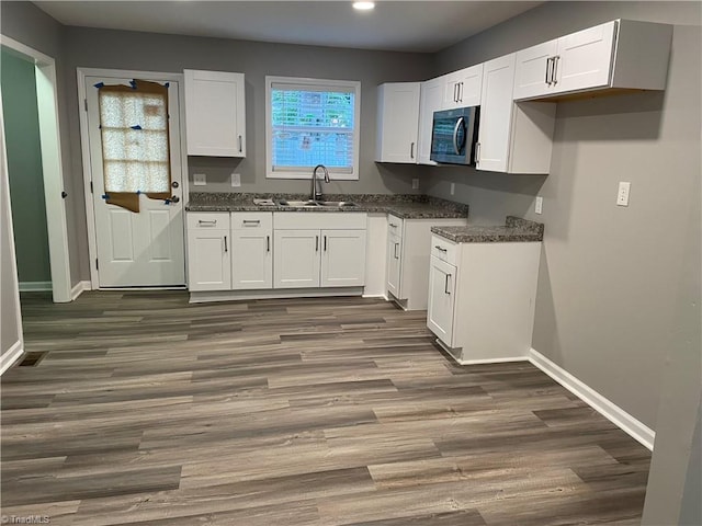 kitchen featuring dark hardwood / wood-style floors, white cabinetry, sink, and dark stone countertops