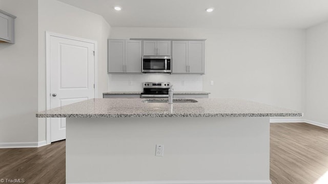6601 Grogan Hill Rd, Whitsett, NC 27377 - kitchen featuring appliances with stainless steel finishes, gray cabinets, dark wood-style floors, light stone countertops, and a center island with sink