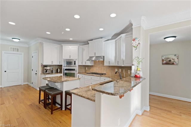 kitchen featuring light hardwood / wood-style flooring, stainless steel appliances, crown molding, a kitchen bar, and white cabinetry