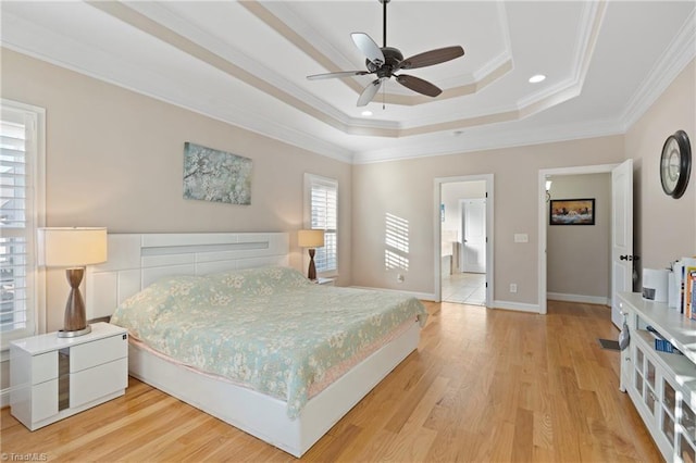 bedroom featuring light hardwood / wood-style flooring, a tray ceiling, ensuite bath, ornamental molding, and ceiling fan