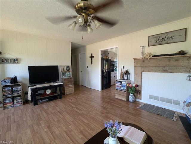 living room featuring ceiling fan, hardwood / wood-style floors, and a textured ceiling