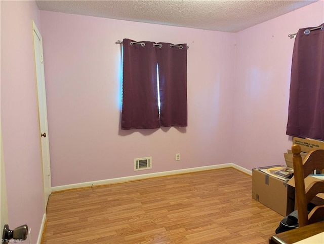 spare room with light wood-type flooring and a textured ceiling