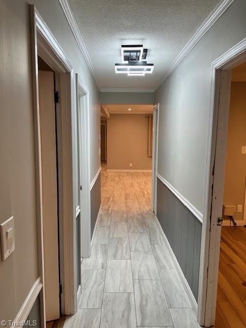 hall with a wainscoted wall, crown molding, and a textured ceiling