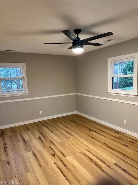 spare room with baseboards, ceiling fan, visible vents, and light wood-type flooring