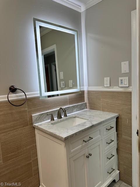 bathroom with tile walls, ornamental molding, vanity, and wainscoting