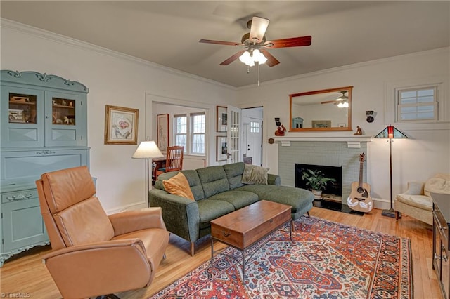 living area with a brick fireplace, ornamental molding, light wood-style floors, and ceiling fan