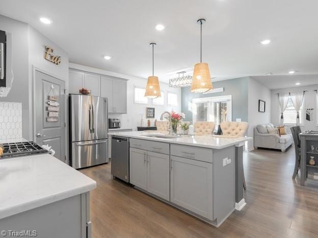 kitchen with sink, gray cabinetry, hanging light fixtures, a kitchen island with sink, and stainless steel appliances