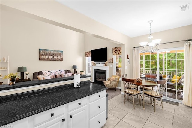 kitchen with a chandelier, a glass covered fireplace, dark countertops, white cabinets, and open floor plan