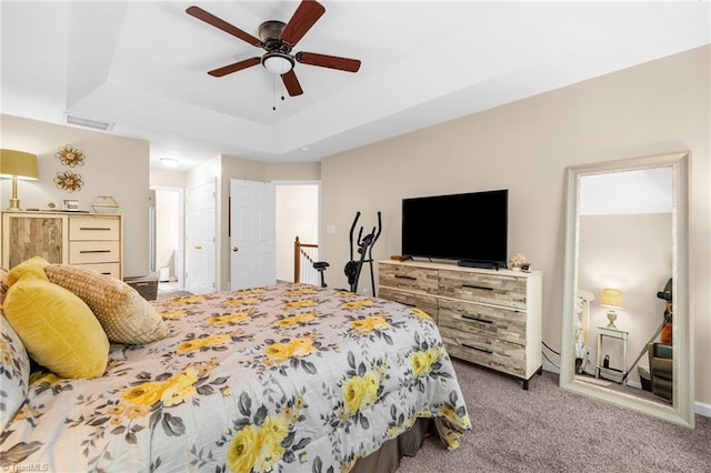 carpeted bedroom featuring a tray ceiling, a ceiling fan, and connected bathroom