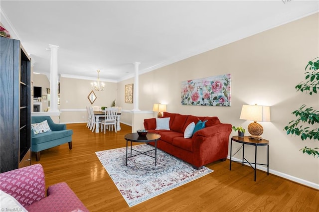 living area featuring ornate columns, wood finished floors, baseboards, a chandelier, and crown molding