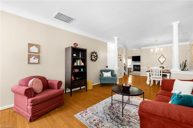 living area featuring ornate columns, ornamental molding, light wood-type flooring, a chandelier, and baseboards