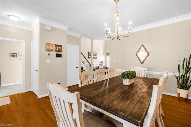 dining space with a chandelier, ornamental molding, wood finished floors, baseboards, and stairway