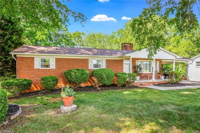 ranch-style house featuring a chimney, brick siding, a front yard, and covered porch
