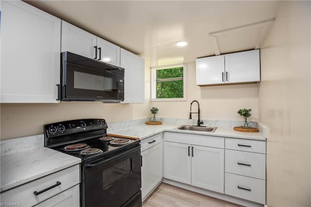 kitchen with black appliances, a sink, white cabinets, light wood-style flooring, and light stone countertops