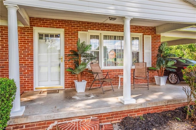 view of exterior entry with a porch and brick siding