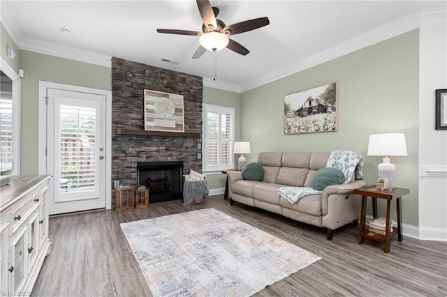 living room featuring crown molding, a healthy amount of sunlight, dark hardwood / wood-style floors, and a stone fireplace