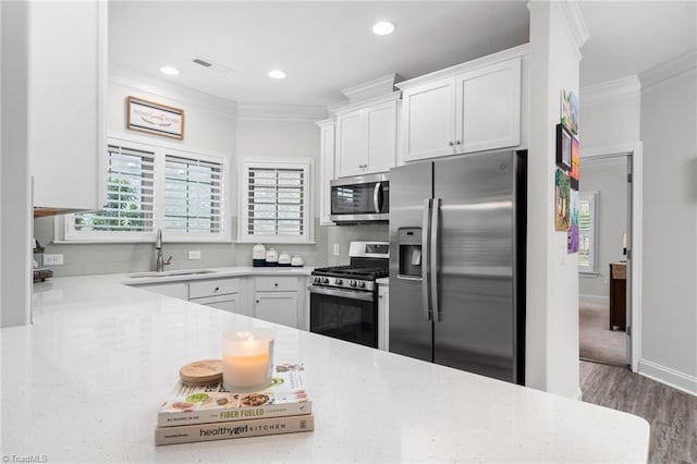 kitchen featuring sink, wood-type flooring, ornamental molding, appliances with stainless steel finishes, and white cabinets