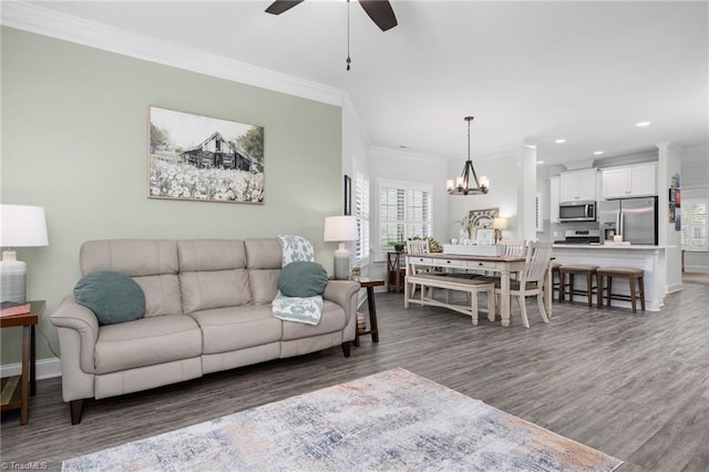 living room featuring ceiling fan with notable chandelier, dark wood-type flooring, and ornamental molding