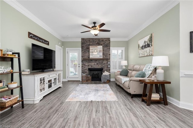 living room with crown molding, hardwood / wood-style flooring, a stone fireplace, and ceiling fan