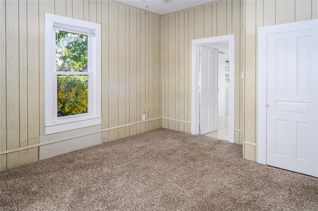 carpeted empty room featuring wood walls