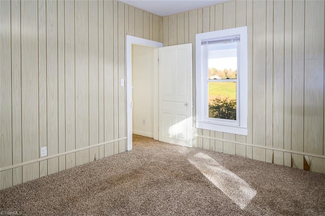 carpeted spare room featuring wood walls