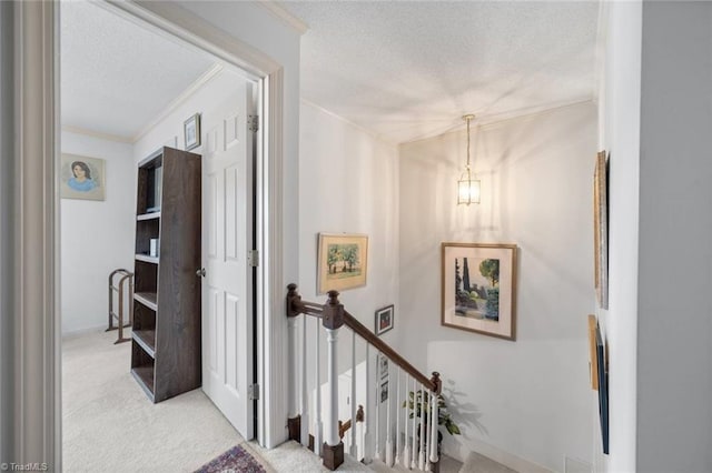 corridor featuring a textured ceiling, an upstairs landing, ornamental molding, carpet floors, and a chandelier
