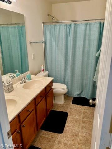 bathroom featuring double vanity, a sink, toilet, and a shower with curtain