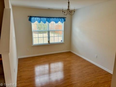 unfurnished dining area with baseboards, wood finished floors, and an inviting chandelier