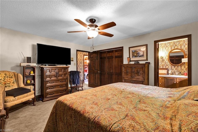 bedroom with ensuite bathroom, a closet, a textured ceiling, light carpet, and ceiling fan