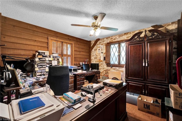 office area with wooden walls, carpet, ceiling fan, and a textured ceiling