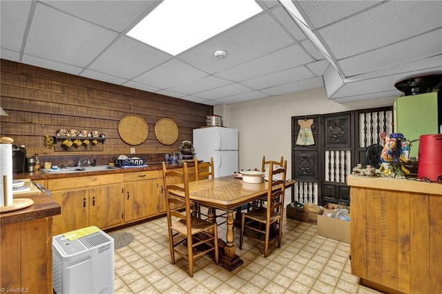 tiled dining room featuring a drop ceiling, wooden walls, and sink