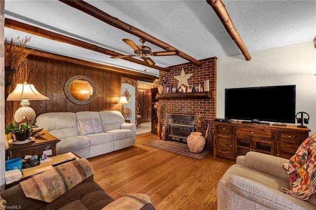 living room with beam ceiling, light wood-type flooring, ceiling fan, brick wall, and a fireplace