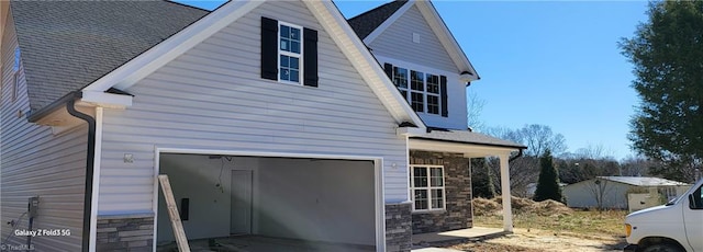 view of side of property with stone siding, an attached garage, and a shingled roof