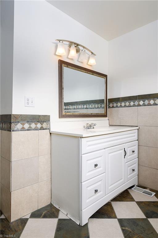 1309 Jackson St, Burlington, NC 27217 - bathroom with tile walls, a wainscoted wall, vanity, and tile patterned floors