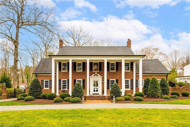 greek revival house with brick siding, a chimney, and a front lawn