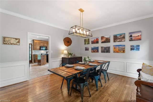 641 Doe Run Dr, Kernersville, NC 27284 - dining space with crown molding, light wood-type flooring, a chandelier, wainscoting, and a decorative wall