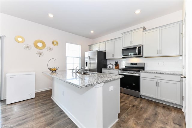 kitchen with a kitchen island with sink, dark wood-type flooring, sink, light stone counters, and stainless steel appliances