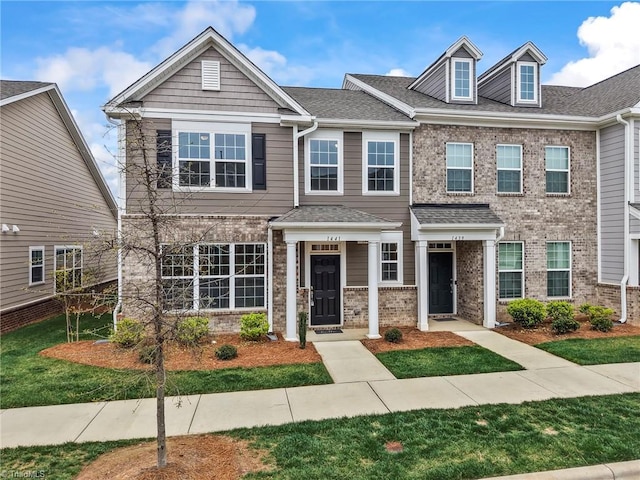 multi unit property with brick siding, a shingled roof, and a front lawn