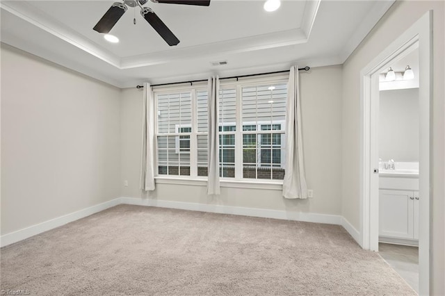 carpeted spare room featuring a tray ceiling, baseboards, visible vents, and ceiling fan