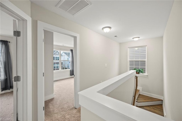 hallway with baseboards, an upstairs landing, visible vents, and light carpet