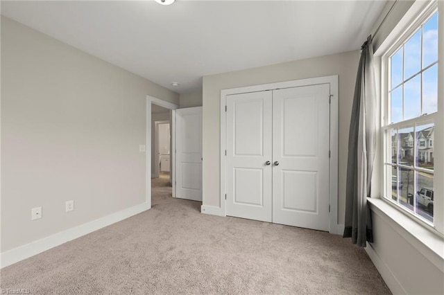 unfurnished bedroom with light colored carpet, a closet, and baseboards