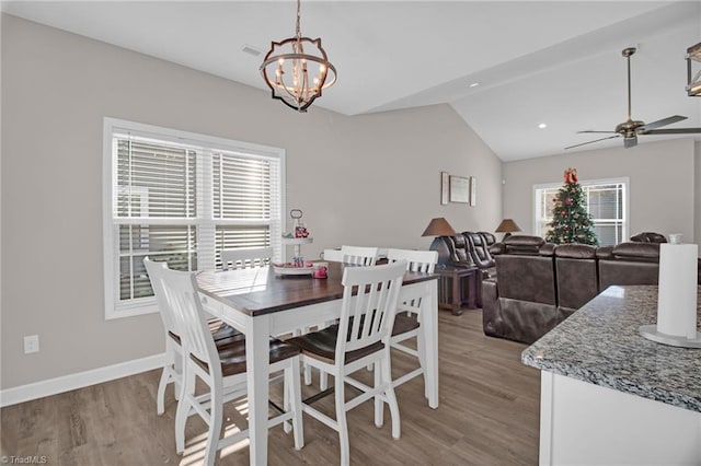 dining area featuring ceiling fan with notable chandelier, vaulted ceiling, and light hardwood / wood-style flooring