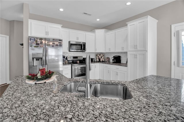 kitchen with tasteful backsplash, white cabinets, dark stone counters, and appliances with stainless steel finishes