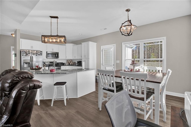 kitchen featuring white cabinets, appliances with stainless steel finishes, decorative light fixtures, and dark stone counters