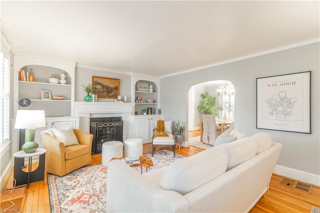 living room with hardwood / wood-style flooring, built in features, ornamental molding, and a chandelier