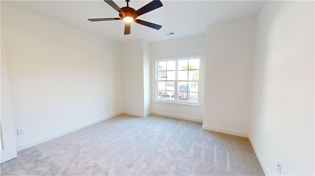 spare room with a ceiling fan, light colored carpet, visible vents, and baseboards