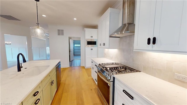 kitchen featuring light stone counters, stainless steel appliances, visible vents, a sink, and wall chimney exhaust hood