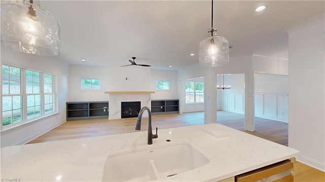 kitchen featuring pendant lighting, a fireplace, open floor plan, a sink, and light stone countertops