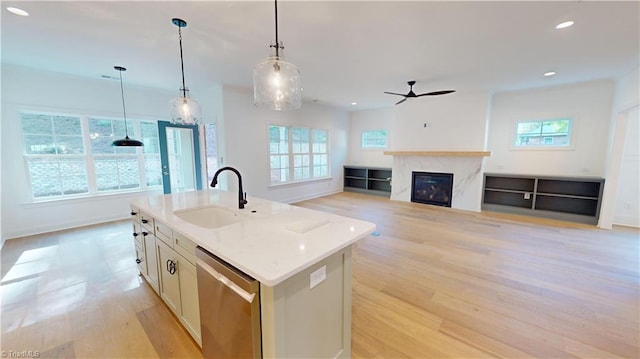 kitchen with a center island with sink, stainless steel dishwasher, open floor plan, a sink, and light stone countertops